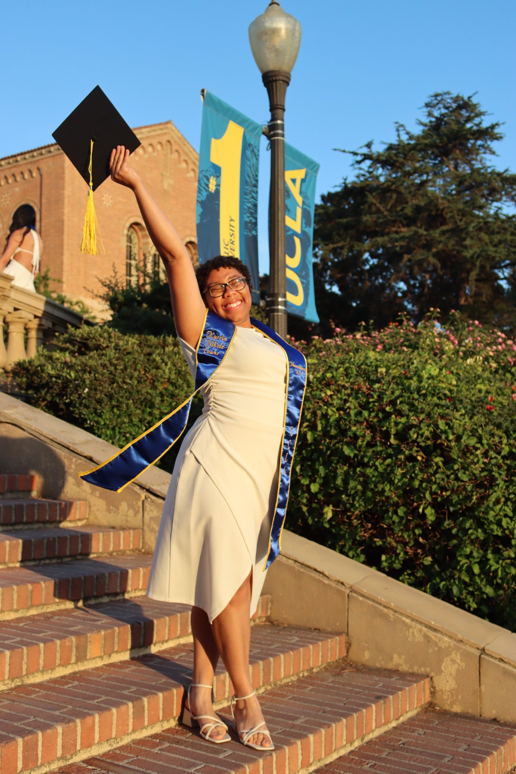 A woman with short hair in a white dress, holding a graduation cap