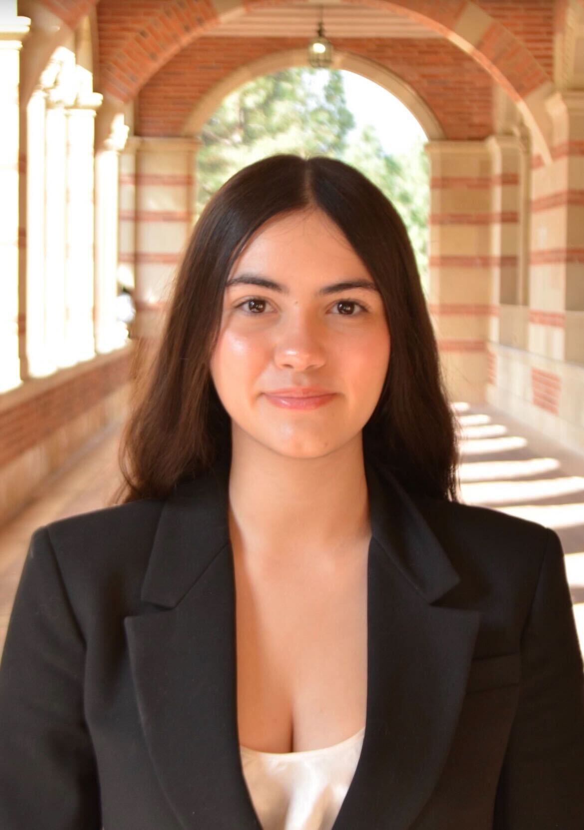 A headshot of a young woman in a suit jacket and blouse, smiling at Royce Hall