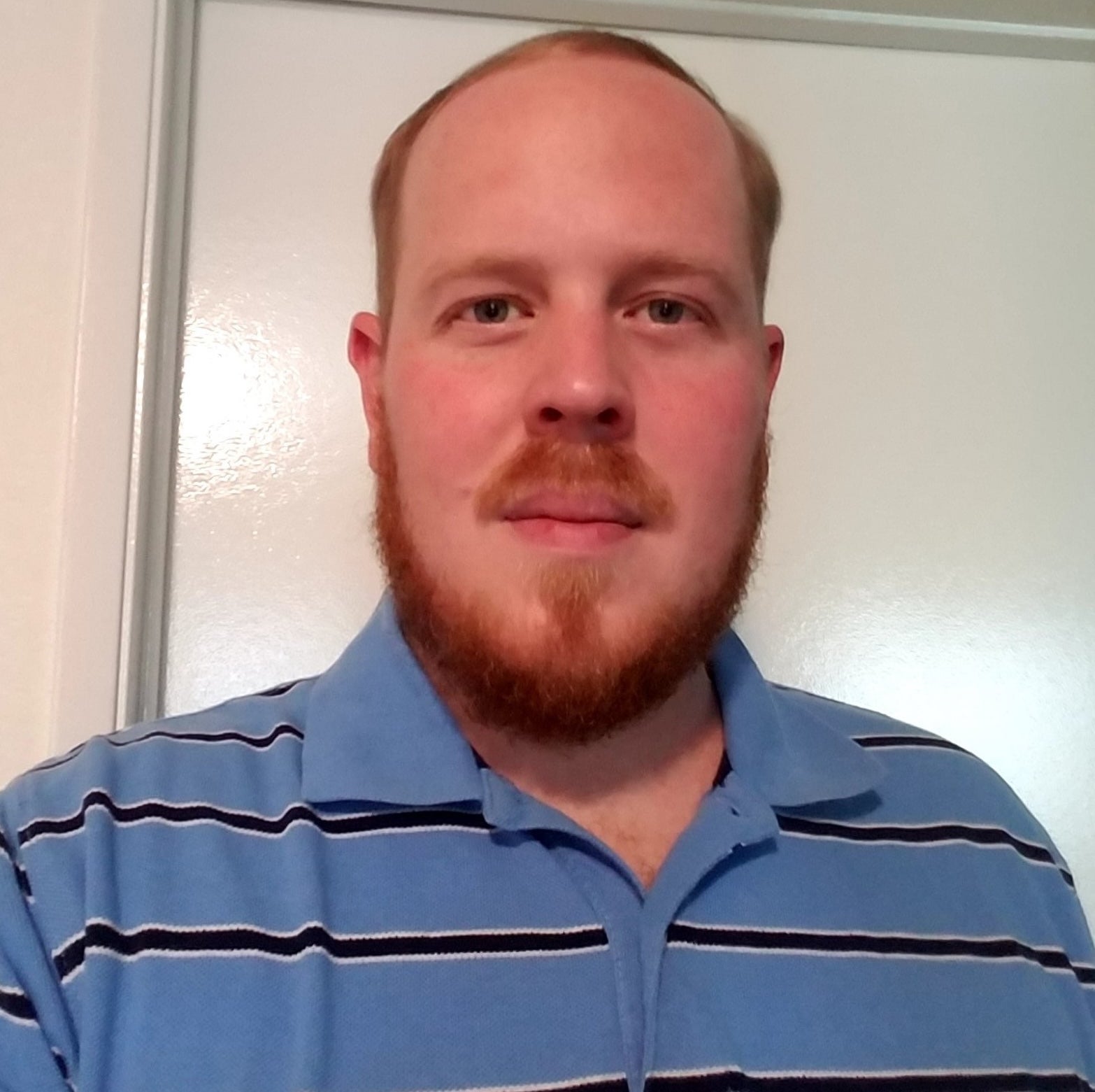 A headshot of a man wearing a blue striped shirt